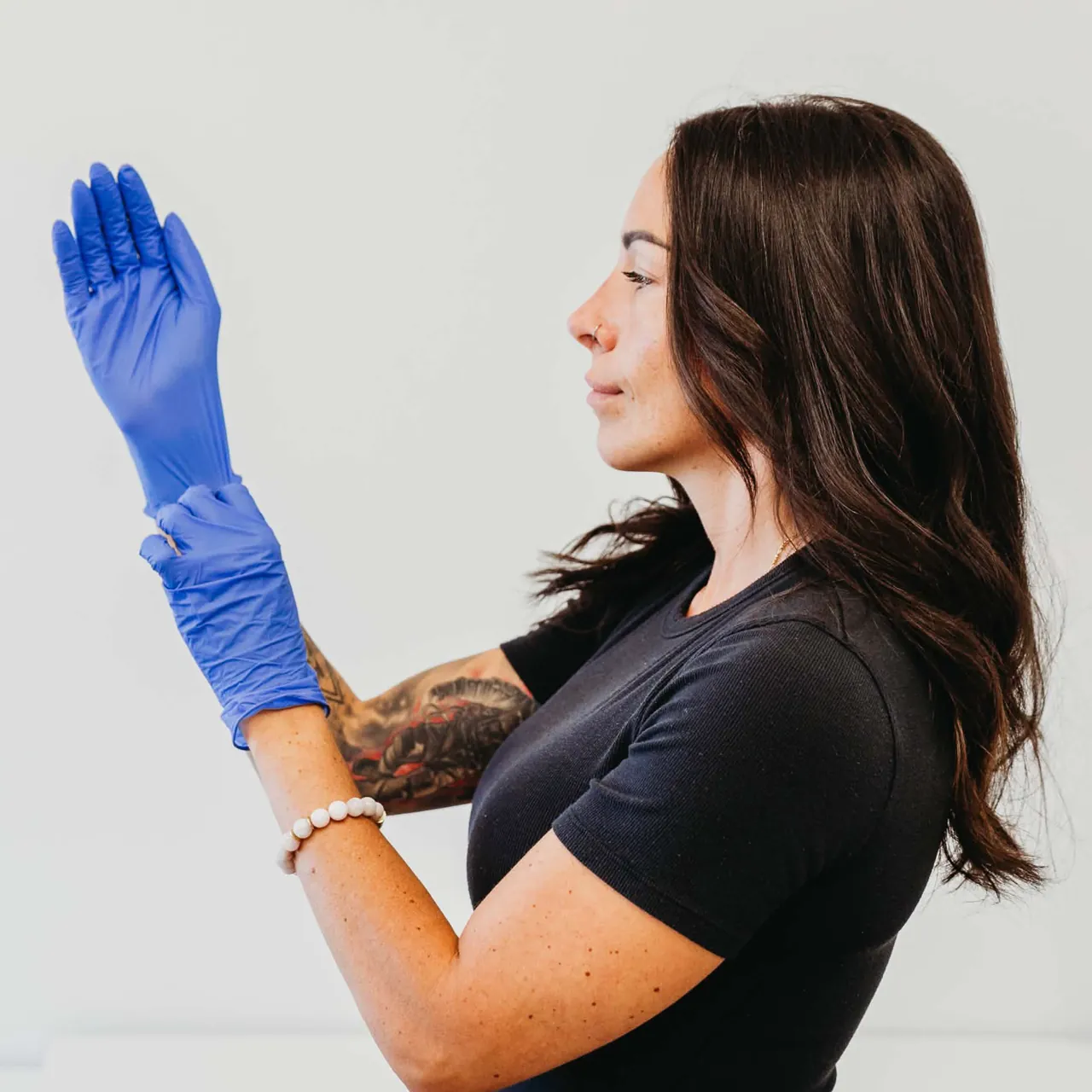 Clare Bourdon in profile, drawing on a clean exam glove before a treatment.